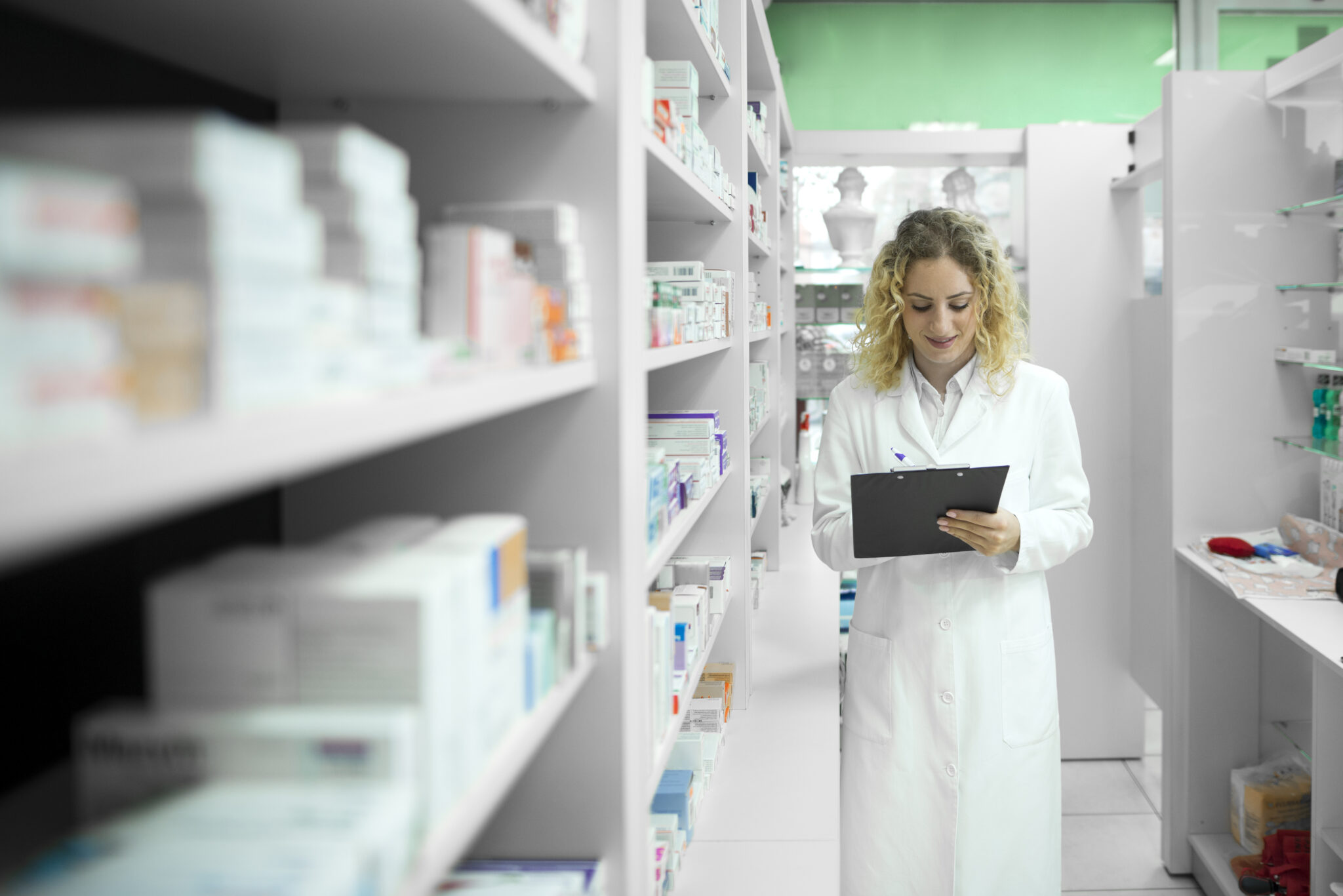 Pharmacist in white uniform walking by the shelf with medicines and checking inventory.
